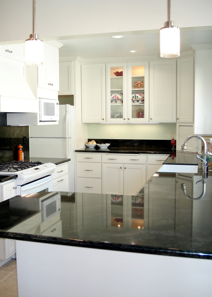 Exempel på ett mellanstort, avskilt klassiskt grön grönt u-kök, med en rustik diskho, luckor med infälld panel, vita skåp, granitbänkskiva, svart stänkskydd, stänkskydd i sten, vita vitvaror, klinkergolv i porslin, en halv köksö och beiget golv