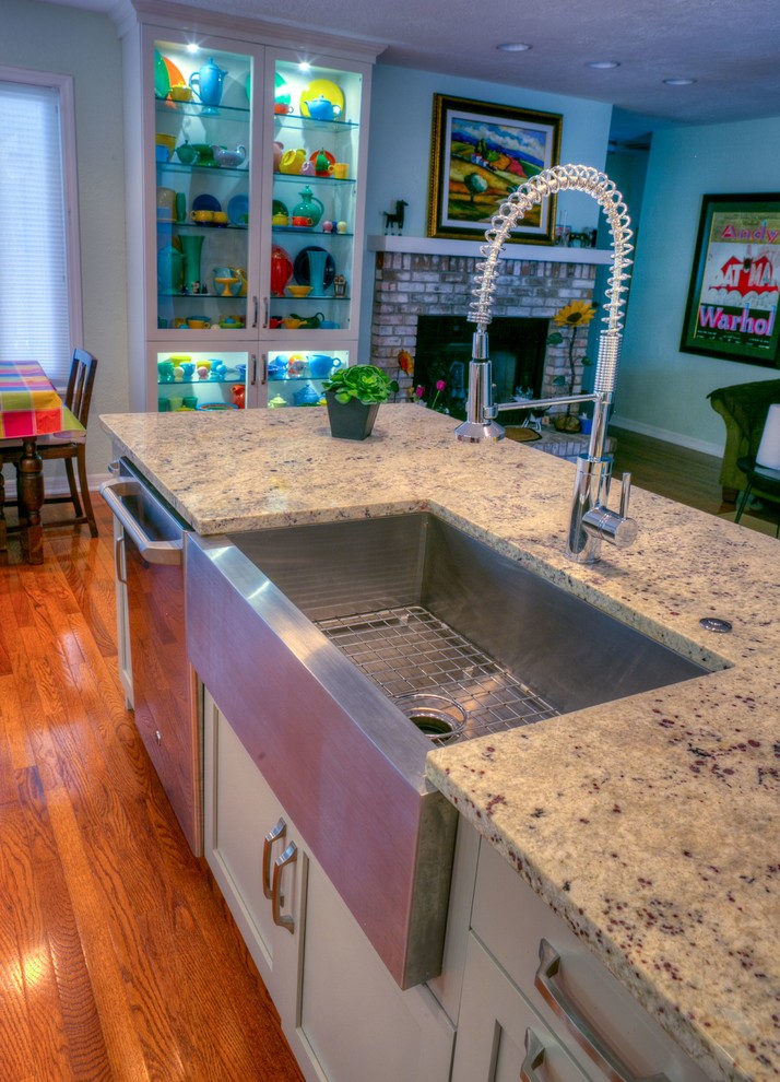 Example of a mid-sized transitional l-shaped light wood floor open concept kitchen design in Orlando with a farmhouse sink, shaker cabinets, beige cabinets, granite countertops, white backsplash, subway tile backsplash, stainless steel appliances and an island