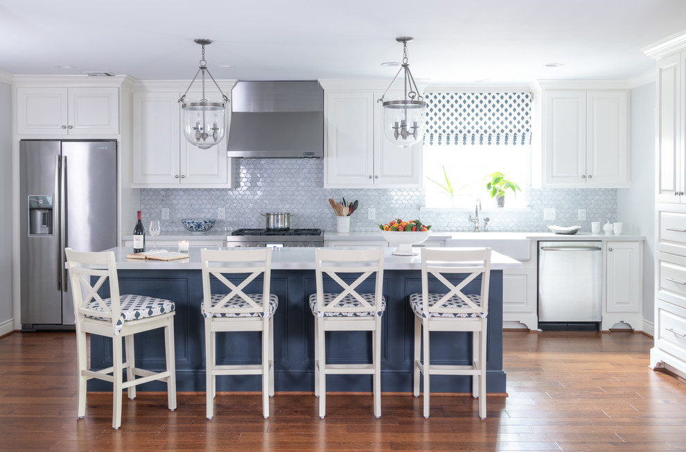Inredning av ett klassiskt vit vitt l-kök, med en rustik diskho, luckor med upphöjd panel, vita skåp, blått stänkskydd, rostfria vitvaror, mellanmörkt trägolv, en köksö och brunt golv