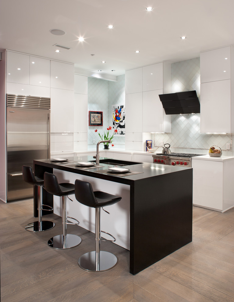 This is an example of a contemporary l-shaped kitchen in Grand Rapids with a submerged sink, flat-panel cabinets, white splashback, stainless steel appliances, light hardwood flooring and an island.
