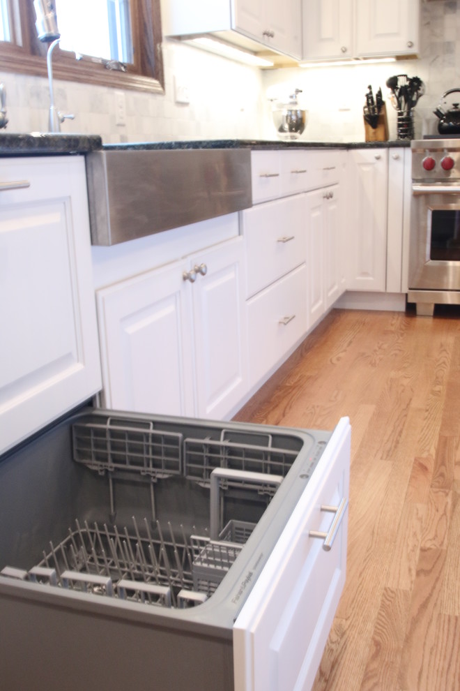 Large farmhouse l-shaped light wood floor and brown floor eat-in kitchen photo in Milwaukee with a farmhouse sink, raised-panel cabinets, white cabinets, granite countertops, white backsplash, marble backsplash, stainless steel appliances and an island