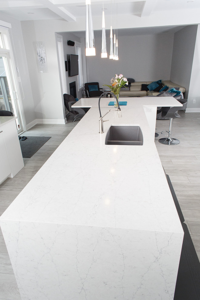 Inspiration for a mid-sized contemporary u-shaped ceramic tile and gray floor kitchen remodel in Ottawa with an undermount sink, flat-panel cabinets, white cabinets, quartz countertops, white backsplash, stainless steel appliances, an island and white countertops