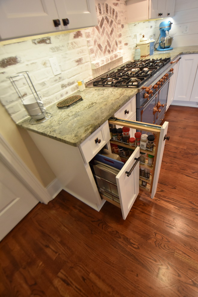 Lantlig inredning av ett mellanstort grön grönt kök, med en rustik diskho, släta luckor, vita skåp, granitbänkskiva, flerfärgad stänkskydd, stänkskydd i tegel, färgglada vitvaror, mellanmörkt trägolv, en halv köksö och brunt golv