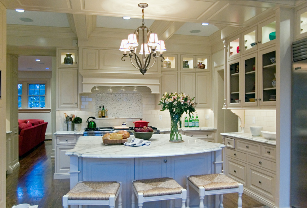 Inredning av ett klassiskt stort u-kök, med en undermonterad diskho, luckor med profilerade fronter, vita skåp, marmorbänkskiva, flerfärgad stänkskydd, stänkskydd i stenkakel, integrerade vitvaror och en köksö