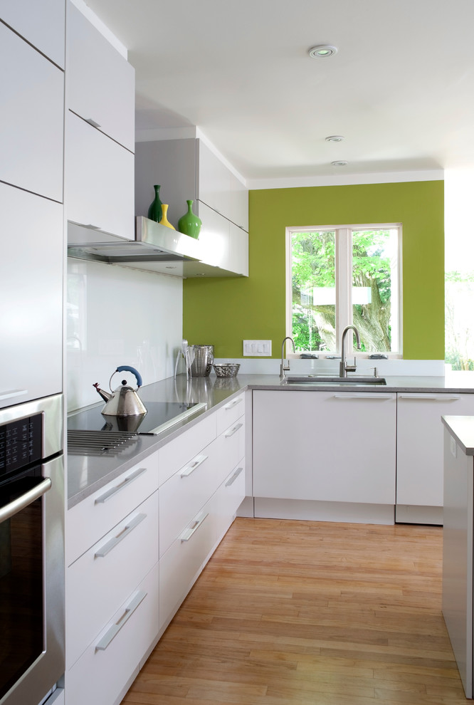 Modern inredning av ett l-kök, med en undermonterad diskho, släta luckor, vita skåp, vitt stänkskydd, rostfria vitvaror, mellanmörkt trägolv och en köksö