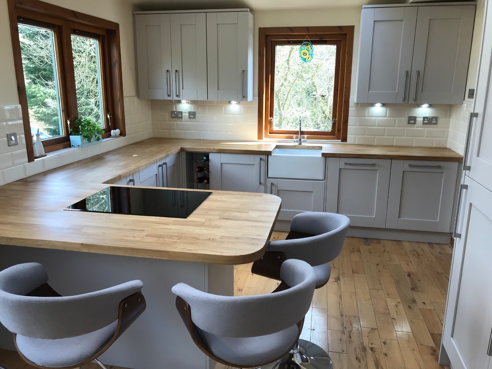 Inspiration for a medium sized traditional l-shaped kitchen/diner in Glasgow with a belfast sink, shaker cabinets, wood worktops, white splashback, metro tiled splashback, black appliances, a breakfast bar, brown floors and brown worktops.