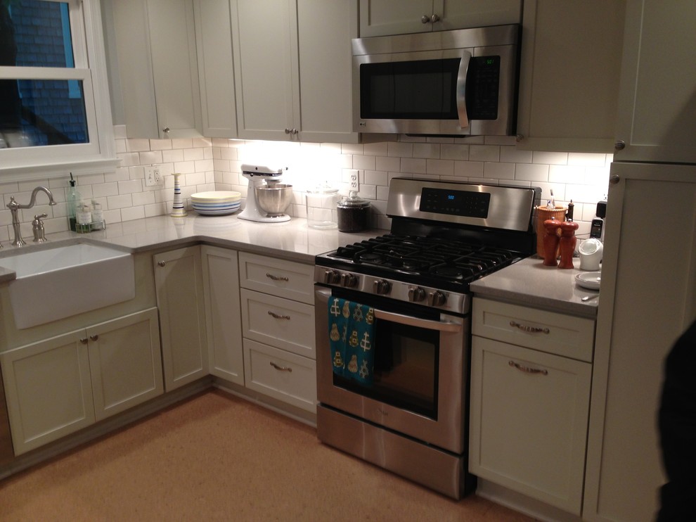 Example of a mid-sized classic l-shaped plywood floor enclosed kitchen design in Baltimore with a farmhouse sink, shaker cabinets, white cabinets, quartz countertops, white backsplash, subway tile backsplash, stainless steel appliances and no island