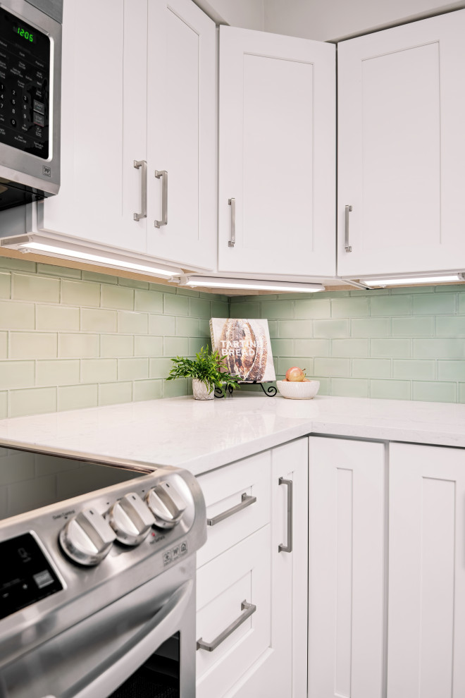Inredning av ett modernt avskilt, mellanstort vit vitt l-kök, med en enkel diskho, skåp i shakerstil, vita skåp, bänkskiva i kvartsit, grönt stänkskydd, stänkskydd i glaskakel, rostfria vitvaror, vinylgolv, en köksö och grått golv