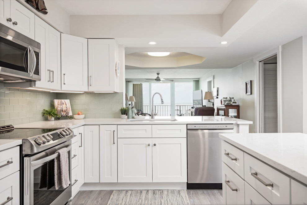 Idéer för att renovera ett avskilt, mellanstort funkis vit vitt l-kök, med en enkel diskho, skåp i shakerstil, vita skåp, bänkskiva i kvartsit, grönt stänkskydd, stänkskydd i glaskakel, rostfria vitvaror, vinylgolv, en köksö och grått golv