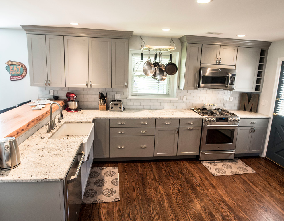 This is an example of a large country l-shaped kitchen/diner in Philadelphia with a belfast sink, shaker cabinets, grey cabinets, wood worktops, grey splashback, glass tiled splashback, stainless steel appliances, medium hardwood flooring and a breakfast bar.