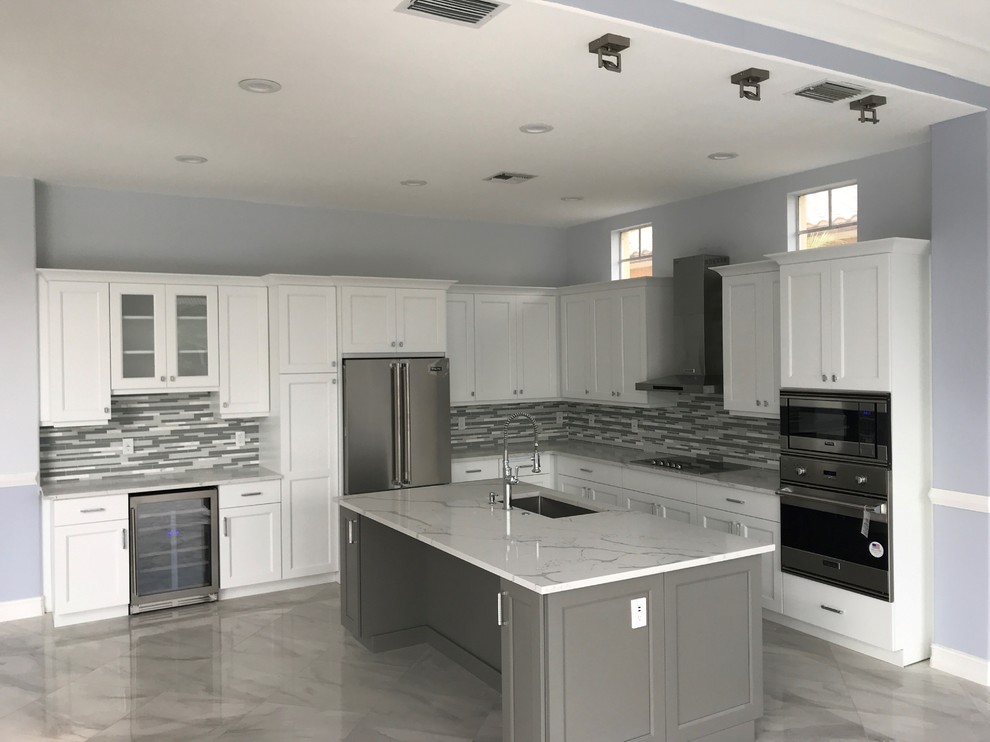 Modern inredning av ett mellanstort vit vitt l-kök, med en undermonterad diskho, skåp i shakerstil, vita skåp, bänkskiva i kvarts, grått stänkskydd, stänkskydd i glaskakel, rostfria vitvaror, marmorgolv, en köksö och vitt golv