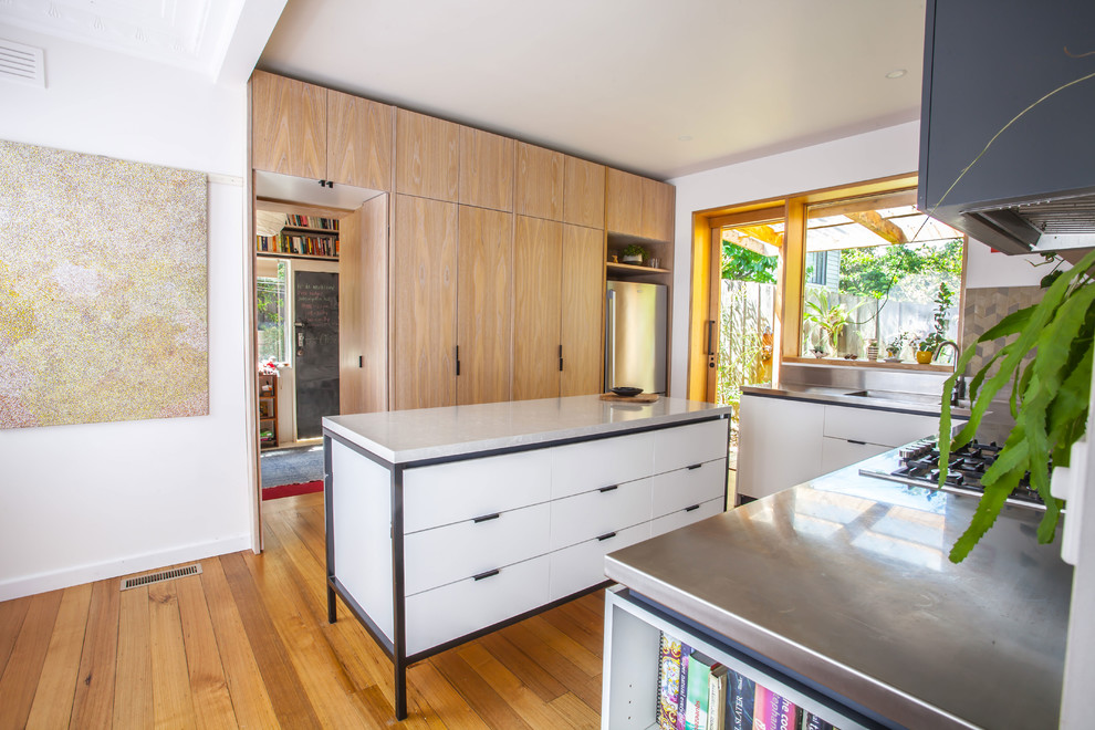 This is an example of a medium sized contemporary u-shaped open plan kitchen in Melbourne with a double-bowl sink, flat-panel cabinets, white cabinets, stainless steel worktops, green splashback, ceramic splashback, stainless steel appliances, medium hardwood flooring and an island.