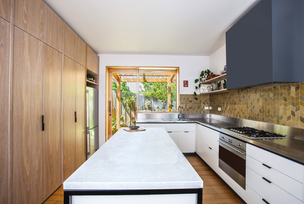 Modern inredning av ett mellanstort kök, med en dubbel diskho, släta luckor, vita skåp, bänkskiva i rostfritt stål, grönt stänkskydd, stänkskydd i keramik, rostfria vitvaror, mellanmörkt trägolv och en köksö