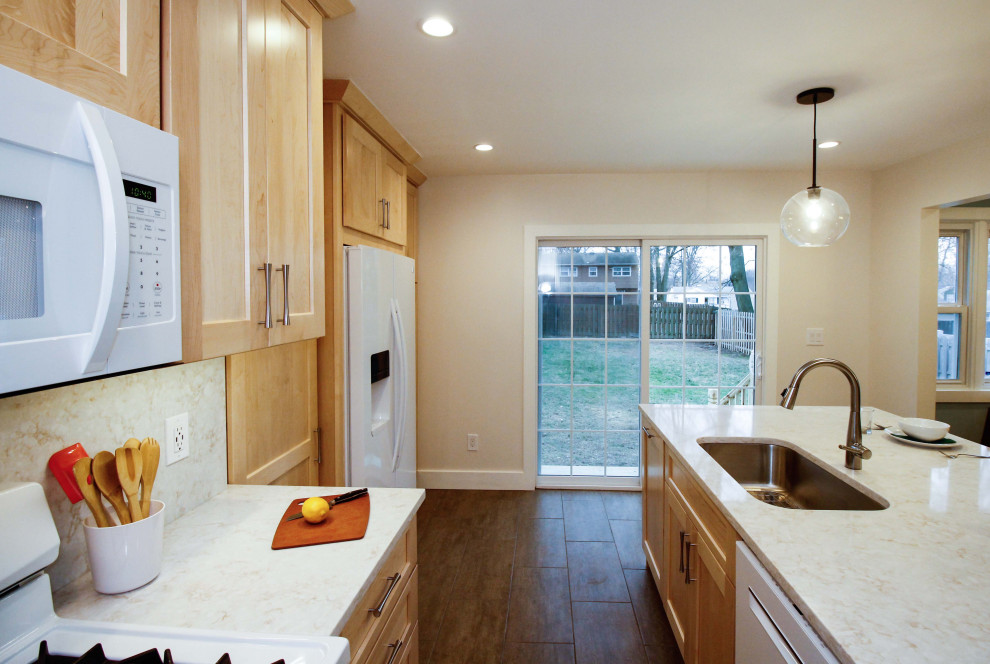 Modern inredning av ett mellanstort vit vitt kök, med en undermonterad diskho, skåp i shakerstil, skåp i ljust trä, bänkskiva i kvarts, vitt stänkskydd, vita vitvaror, klinkergolv i porslin, en köksö och brunt golv