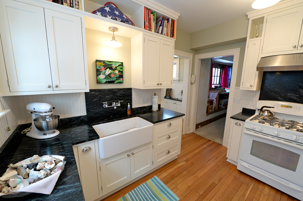 Exempel på ett avskilt, litet lantligt u-kök, med en rustik diskho, skåp i shakerstil, vita skåp, bänkskiva i täljsten, flerfärgad stänkskydd, stänkskydd i sten, vita vitvaror och ljust trägolv