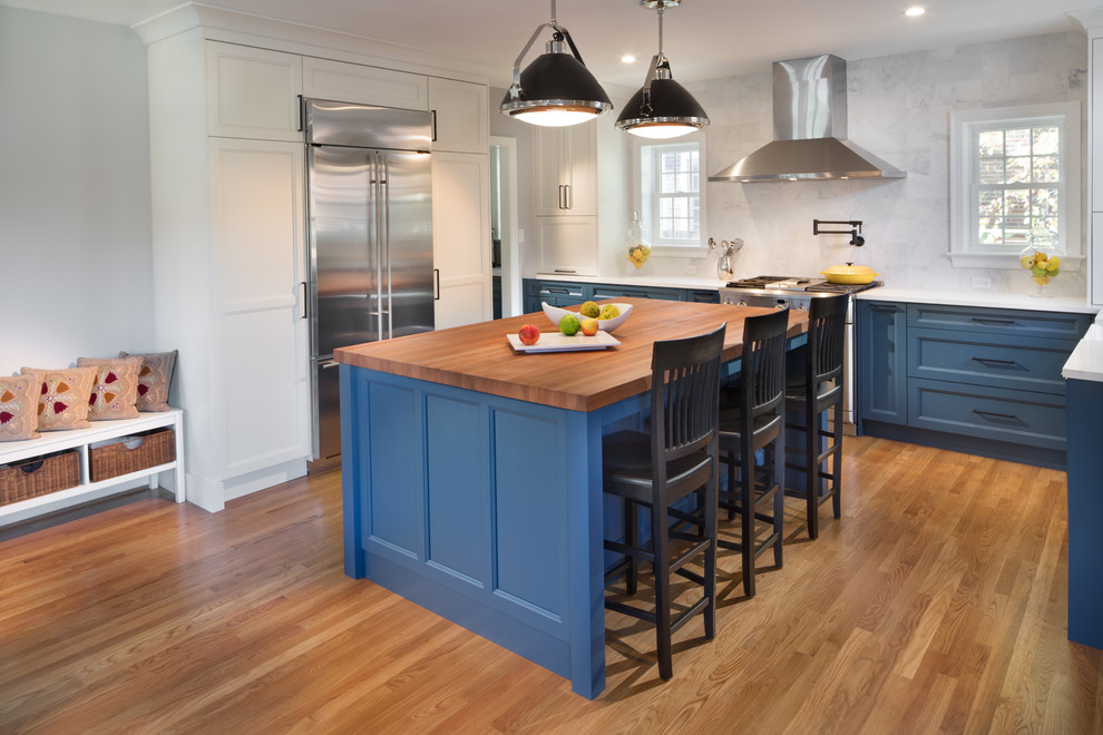 Medium sized classic l-shaped kitchen/diner in DC Metro with a belfast sink, blue cabinets, stone tiled splashback, light hardwood flooring, an island, white splashback, stainless steel appliances, shaker cabinets and engineered stone countertops.