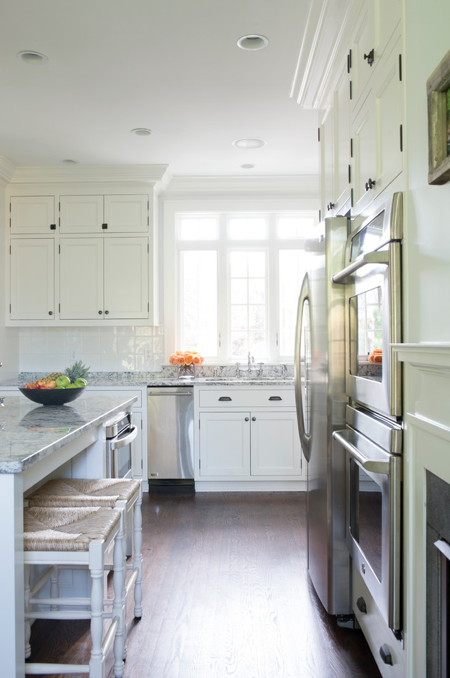 Mittelgroße Klassische Küche mit Schrankfronten im Shaker-Stil, weißen Schränken, Marmor-Arbeitsplatte, Küchenrückwand in Weiß, Rückwand aus Keramikfliesen, dunklem Holzboden und Kücheninsel in New York