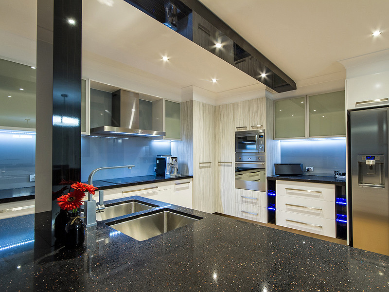 Inspiration for a medium sized contemporary u-shaped kitchen/diner in Gold Coast - Tweed with a double-bowl sink, flat-panel cabinets, white cabinets, granite worktops, blue splashback, glass sheet splashback, stainless steel appliances and light hardwood flooring.