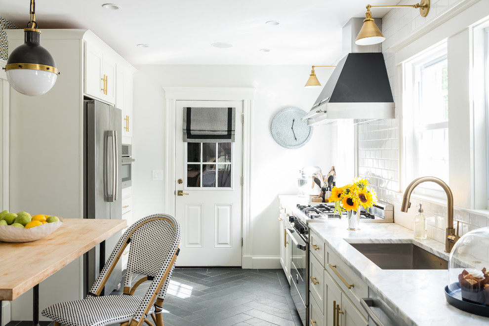 Bild på ett litet vintage kök, med en undermonterad diskho, vita skåp, marmorbänkskiva, vitt stänkskydd, stänkskydd i tunnelbanekakel, rostfria vitvaror, skiffergolv och en köksö