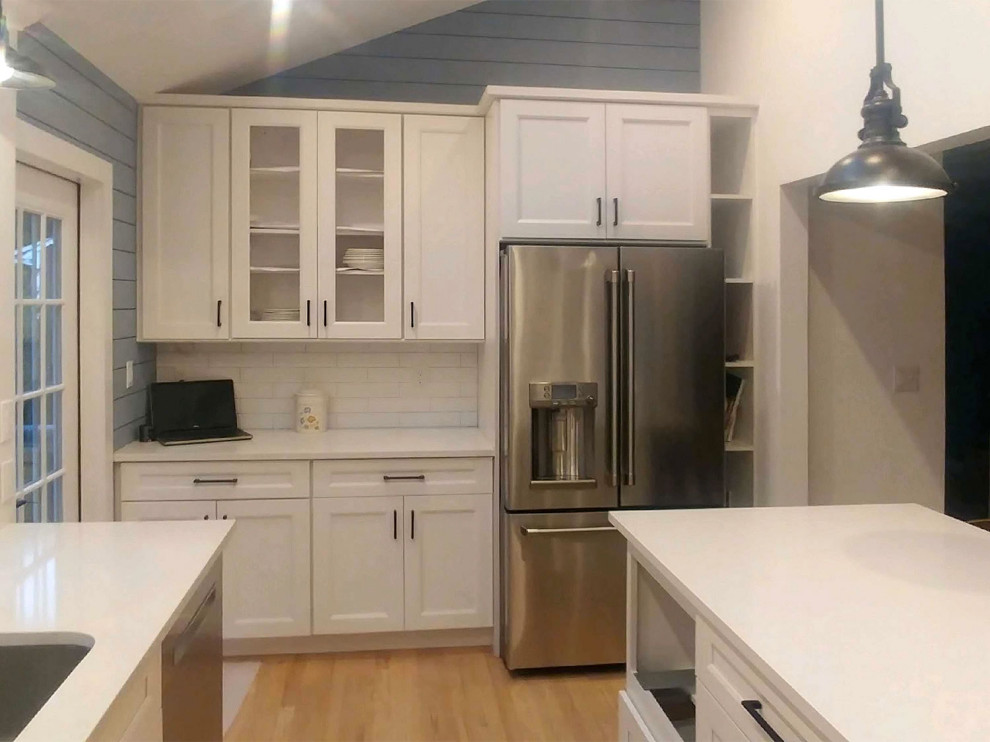 This is an example of a farmhouse kitchen in New York with recessed-panel cabinets, white cabinets, white splashback, stainless steel appliances and an island.