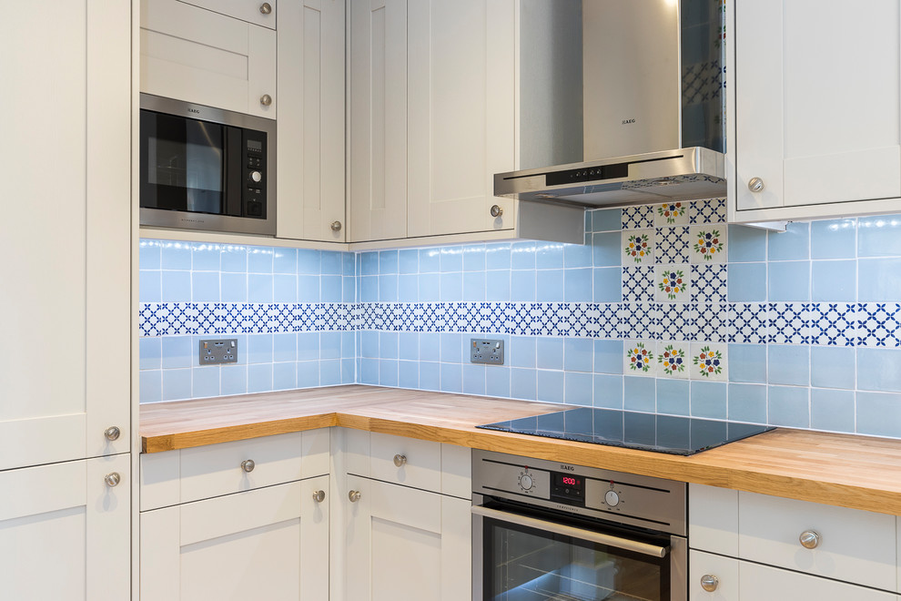 Inspiration for a medium sized vintage u-shaped kitchen/diner in London with a double-bowl sink, raised-panel cabinets, grey cabinets, wood worktops, blue splashback, mosaic tiled splashback, black appliances, cement flooring and no island.