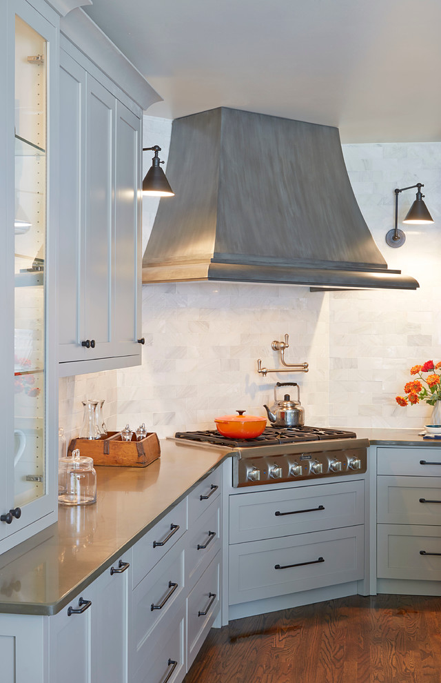 Klassisk inredning av ett mellanstort kök, med en rustik diskho, luckor med infälld panel, vita skåp, bänkskiva i kvarts, vitt stänkskydd, stänkskydd i porslinskakel, rostfria vitvaror, mörkt trägolv och flera köksöar