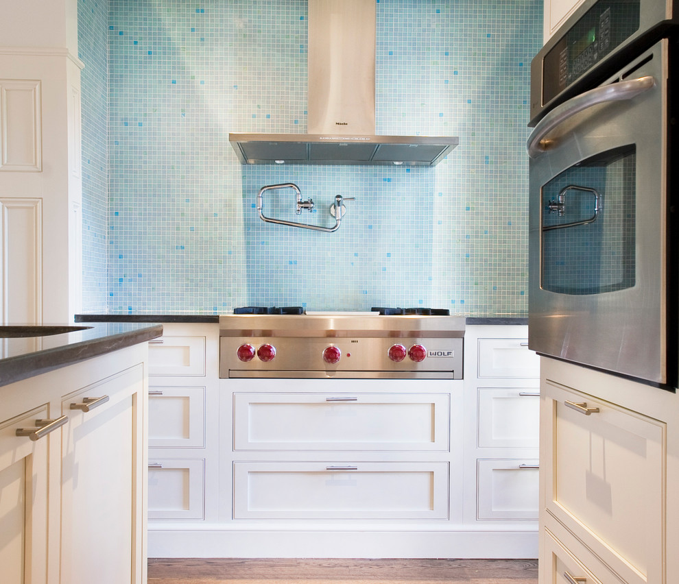 Offene Moderne Küche in U-Form mit Küchengeräten aus Edelstahl, dunklem Holzboden, Kücheninsel, Kassettenfronten, weißen Schränken, Küchenrückwand in Blau, Rückwand aus Mosaikfliesen und Landhausspüle in Sonstige