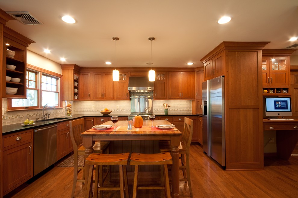 Mid-sized elegant l-shaped medium tone wood floor and brown floor eat-in kitchen photo in New York with recessed-panel cabinets, medium tone wood cabinets, glass tile backsplash, stainless steel appliances, an undermount sink, solid surface countertops, gray backsplash and an island