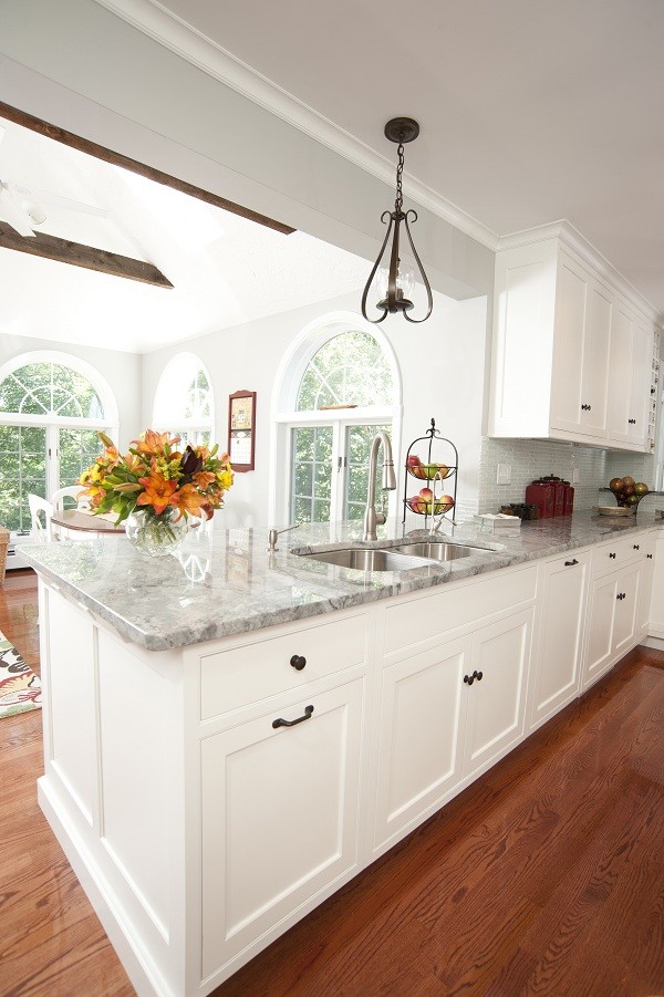 Inspiration for a large timeless medium tone wood floor open concept kitchen remodel in Boston with a double-bowl sink, recessed-panel cabinets, white cabinets, granite countertops, paneled appliances and an island