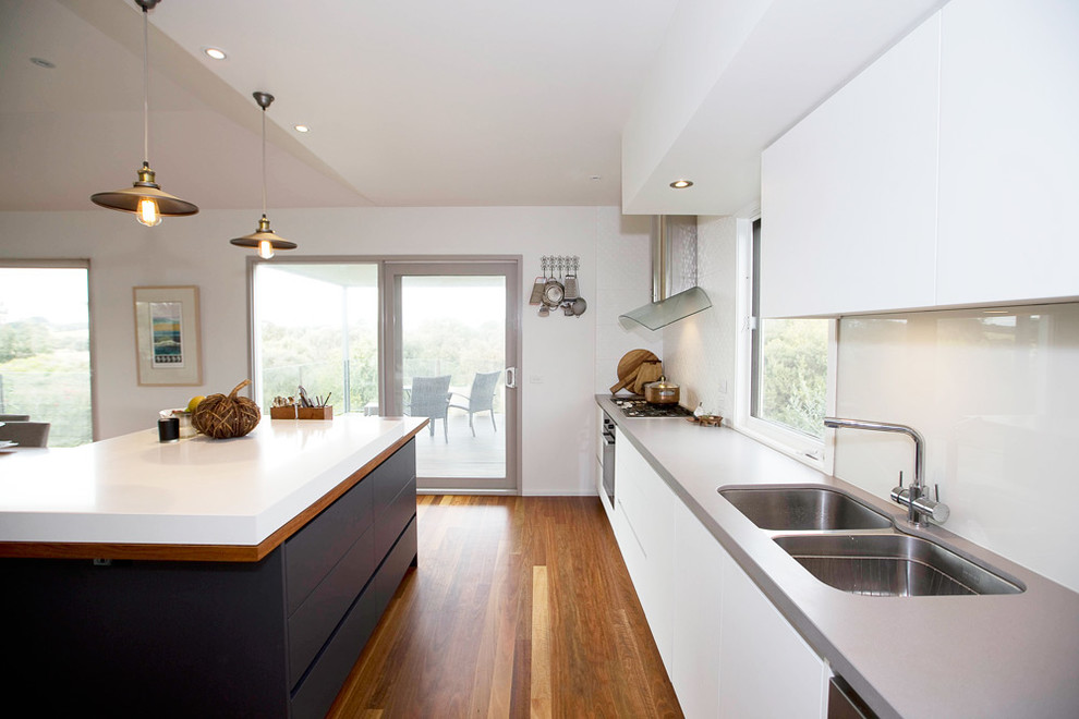 Example of a mid-sized trendy single-wall medium tone wood floor open concept kitchen design in Melbourne with a drop-in sink, quartz countertops, gray backsplash, glass tile backsplash, black appliances and an island