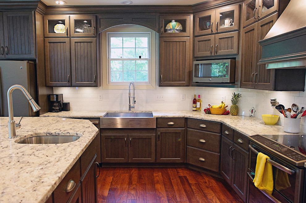Example of a large classic l-shaped dark wood floor and red floor kitchen design in Other with a farmhouse sink, recessed-panel cabinets, dark wood cabinets, granite countertops, white backsplash, subway tile backsplash and an island