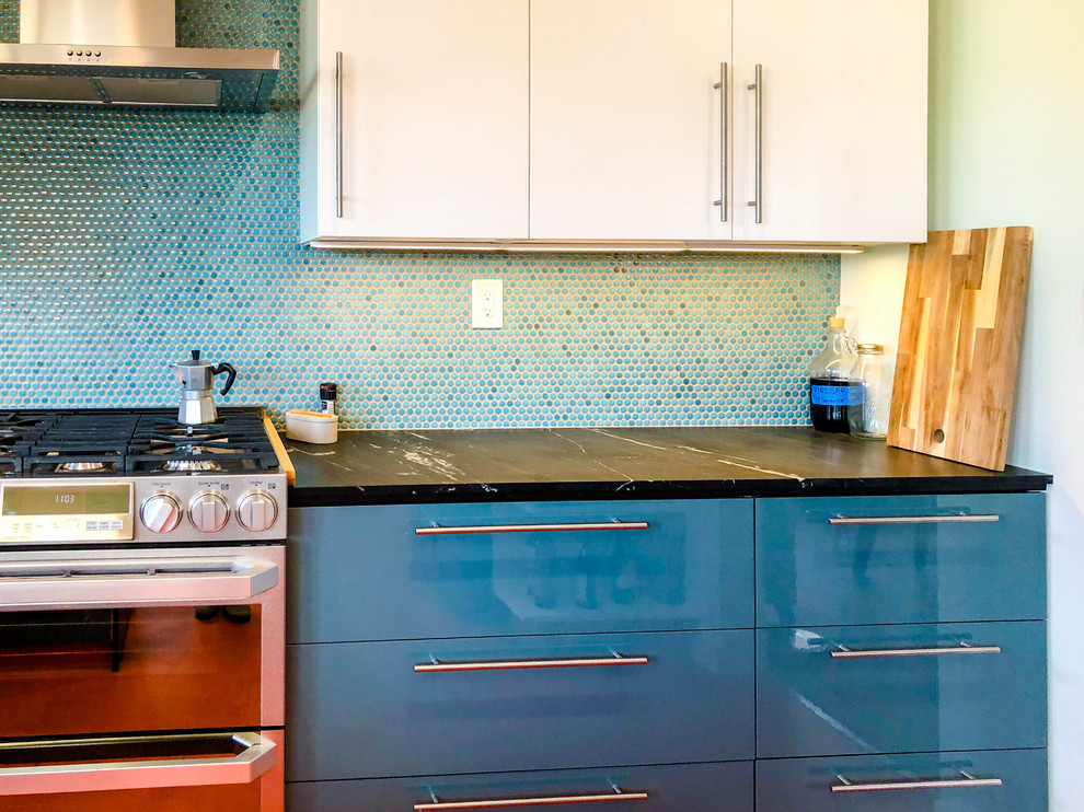 Inredning av ett modernt mellanstort svart svart kök, med släta luckor, vita skåp, blått stänkskydd, rostfria vitvaror, en halv köksö, orange golv, en nedsänkt diskho, granitbänkskiva, stänkskydd i mosaik och vinylgolv