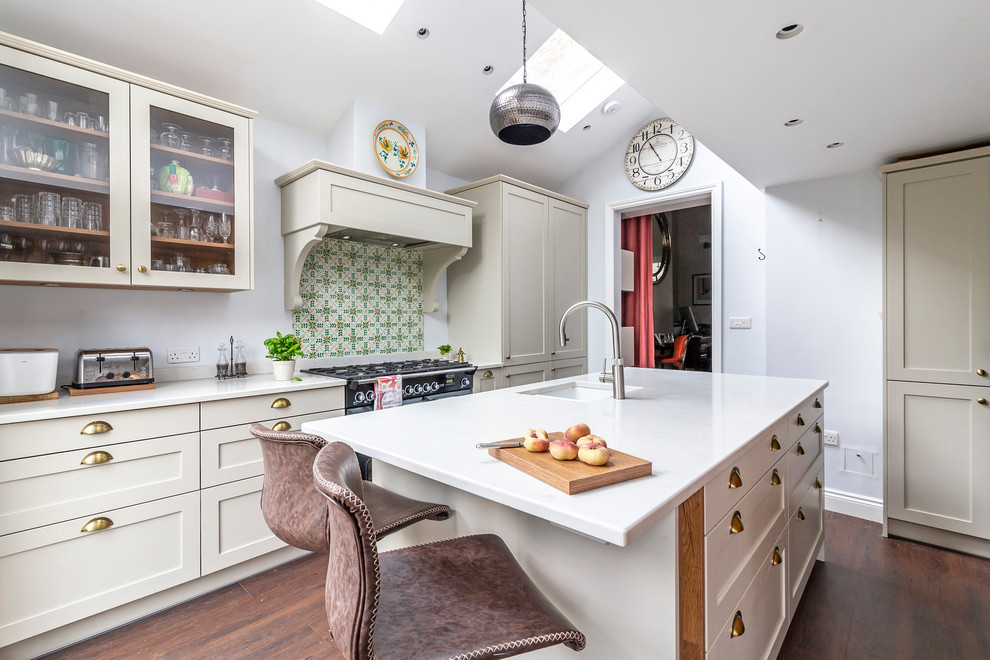 Photo of a classic galley kitchen in London with a submerged sink, shaker cabinets, beige cabinets, multi-coloured splashback, stainless steel appliances, dark hardwood flooring, an island, brown floors and white worktops.