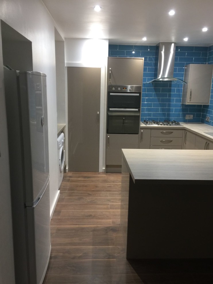 Example of a mid-sized trendy u-shaped laminate floor eat-in kitchen design in London with an integrated sink, flat-panel cabinets, gray cabinets, laminate countertops, blue backsplash, ceramic backsplash, stainless steel appliances and no island