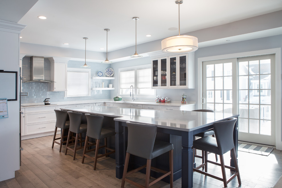Mid-sized transitional u-shaped medium tone wood floor eat-in kitchen photo in Boston with an undermount sink, shaker cabinets, white cabinets, solid surface countertops, blue backsplash, glass tile backsplash, stainless steel appliances and an island