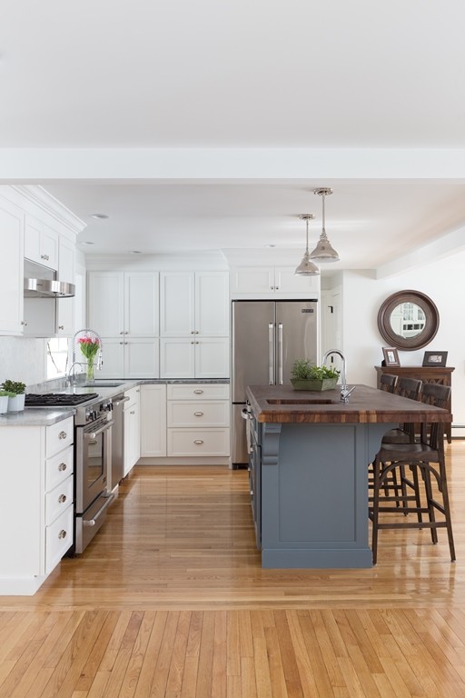 Example of a small transitional l-shaped light wood floor eat-in kitchen design in Boston with an undermount sink, shaker cabinets, white cabinets, granite countertops, white backsplash, mosaic tile backsplash, stainless steel appliances and an island