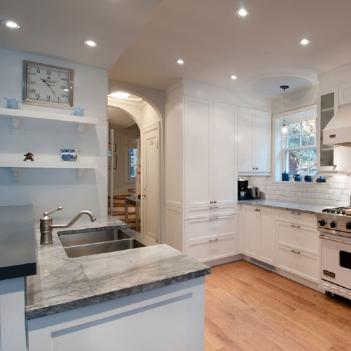 Design ideas for a medium sized contemporary l-shaped kitchen/diner in Montreal with a belfast sink, shaker cabinets, white cabinets, marble worktops, white splashback, ceramic splashback, integrated appliances, light hardwood flooring and a breakfast bar.