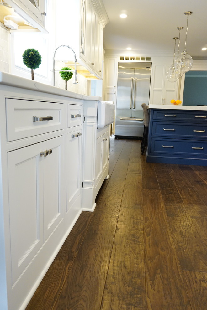 Klassisk inredning av ett mellanstort kök, med en rustik diskho, luckor med profilerade fronter, vita skåp, bänkskiva i kvartsit, grått stänkskydd, stänkskydd i marmor, rostfria vitvaror, mörkt trägolv, en köksö och brunt golv