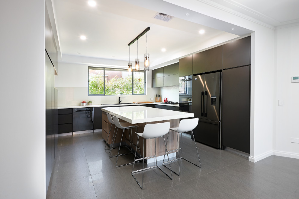 Example of a minimalist u-shaped porcelain tile and gray floor enclosed kitchen design in Melbourne with a drop-in sink, flat-panel cabinets, black cabinets, quartz countertops, white backsplash, glass sheet backsplash, black appliances, an island and white countertops