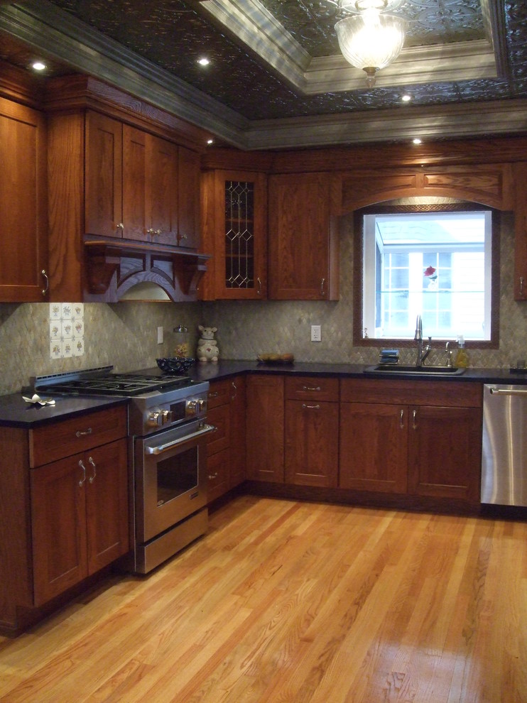 Cette image montre une cuisine américaine traditionnelle en U et bois brun avec un évier posé, un placard avec porte à panneau encastré, un plan de travail en quartz, une crédence grise, une crédence en mosaïque et un électroménager en acier inoxydable.