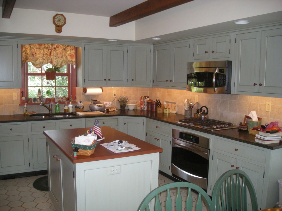 Photo of a large rural l-shaped kitchen/diner in Philadelphia with a double-bowl sink, recessed-panel cabinets, green cabinets, granite worktops, beige splashback, stone tiled splashback, stainless steel appliances, porcelain flooring and an island.