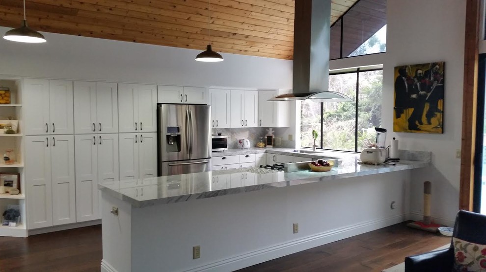 Bild på ett funkis u-kök, med skåp i shakerstil, vita skåp, bänkskiva i kvartsit, stänkskydd i sten, rostfria vitvaror, mörkt trägolv och en halv köksö