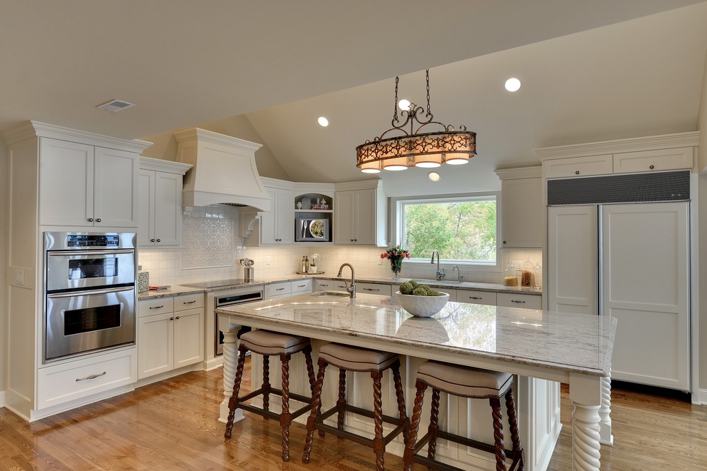 Large classic l-shaped kitchen/diner in Minneapolis with a submerged sink, white cabinets, white appliances, an island, white splashback, ceramic splashback, granite worktops, brown floors, recessed-panel cabinets and medium hardwood flooring.