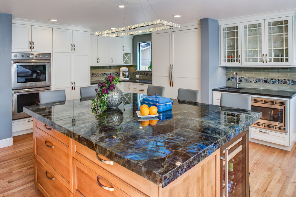 Large classic kitchen in San Francisco with a submerged sink, shaker cabinets, white cabinets, grey splashback, glass tiled splashback, stainless steel appliances, light hardwood flooring and an island.