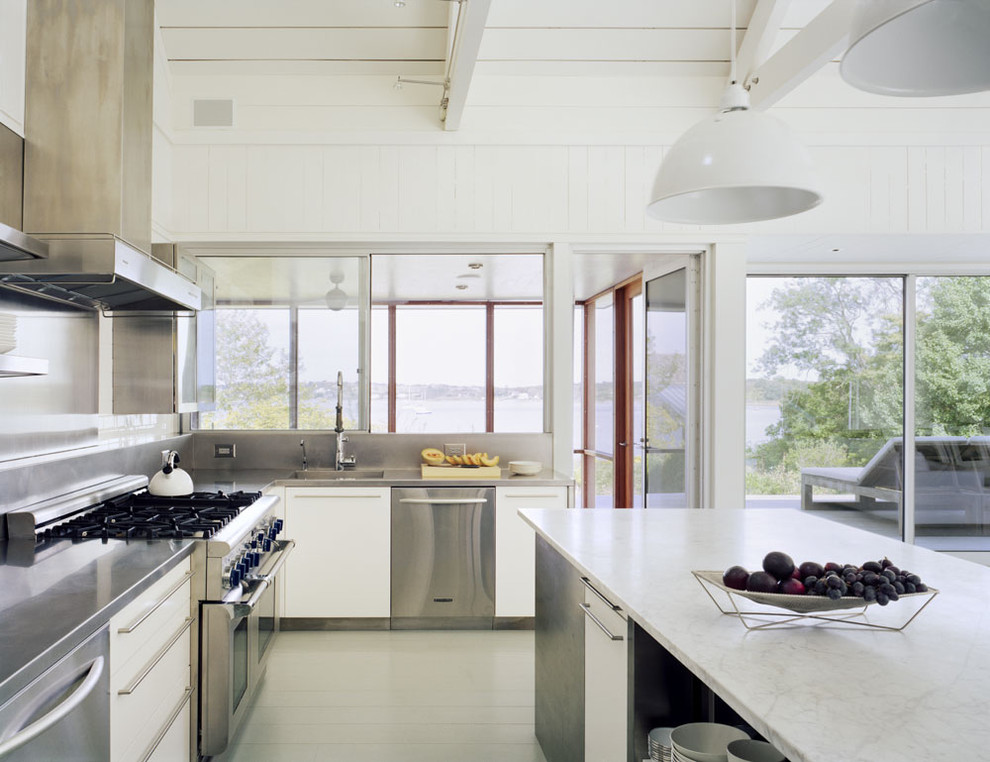 Foto på ett maritimt kök, med släta luckor, vita skåp, bänkskiva i rostfritt stål, stänkskydd med metallisk yta, rostfria vitvaror, en integrerad diskho och stänkskydd i metallkakel