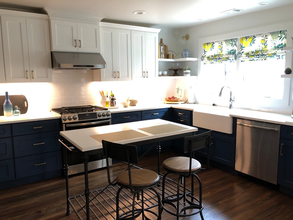 Amerikansk inredning av ett mellanstort vit vitt l-kök, med en rustik diskho, skåp i shakerstil, blå skåp, bänkskiva i kvartsit, vitt stänkskydd, stänkskydd i tunnelbanekakel, rostfria vitvaror och en köksö