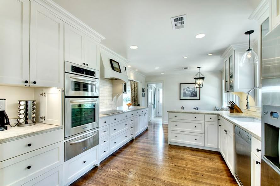 Example of a mid-sized l-shaped medium tone wood floor enclosed kitchen design in Houston with a drop-in sink, recessed-panel cabinets, white cabinets, limestone countertops, white backsplash, subway tile backsplash, stainless steel appliances and a peninsula