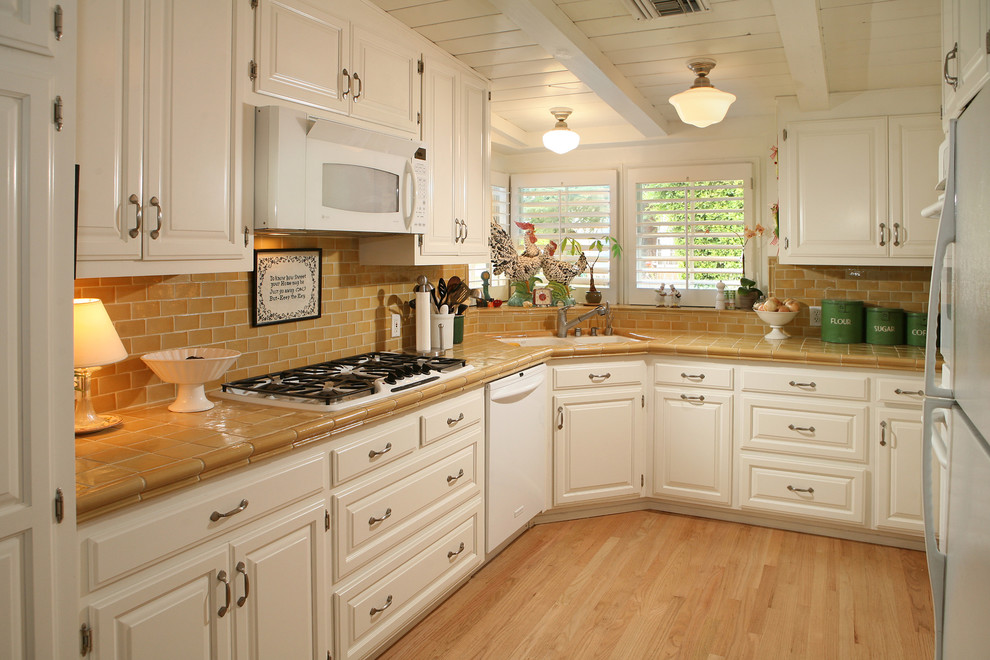 Пример оригинального дизайна: отдельная кухня в классическом стиле с столешницей из плитки, белой техникой, фасадами с выступающей филенкой, белыми фасадами, коричневым фартуком и фартуком из плитки кабанчик