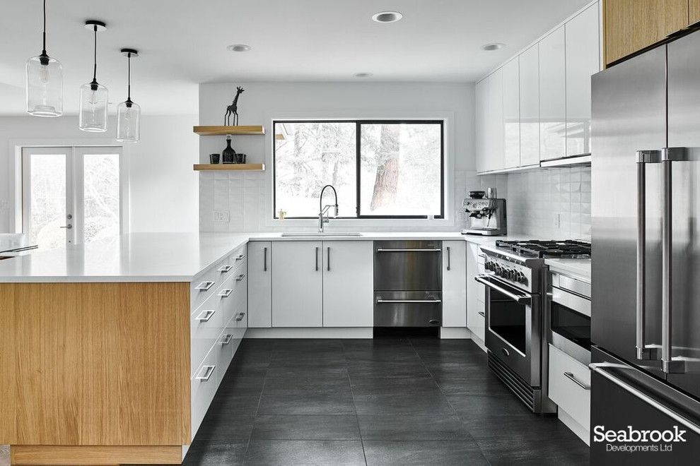 This is an example of a medium sized contemporary u-shaped kitchen/diner in Vancouver with a submerged sink, flat-panel cabinets, white cabinets, engineered stone countertops, white splashback, ceramic splashback, stainless steel appliances, slate flooring, a breakfast bar, black floors and white worktops.