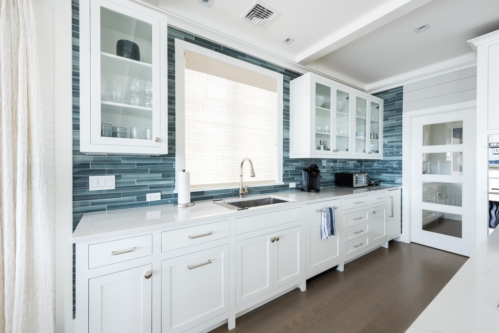 Mid-sized beach style l-shaped medium tone wood floor and brown floor open concept kitchen photo in New York with an undermount sink, white cabinets, quartz countertops, blue backsplash, glass tile backsplash, stainless steel appliances, an island, gray countertops and shaker cabinets